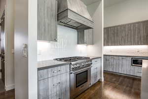 Kitchen featuring custom exhaust hood, dark wood-type flooring, and stainless steel stove