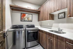 Laundry room with washer and clothes dryer, light tile patterned floors, cabinets, and sink