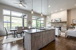 Kitchen featuring sink, dark hardwood / wood-style floors, pendant lighting, a kitchen island with sink, and a fireplace