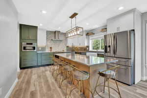 Kitchen with light wood-type flooring, appliances with stainless steel finishes, a center island, and wall chimney range hood