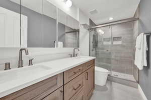 Bathroom featuring a shower with door, vanity, toilet, and tile patterned floors