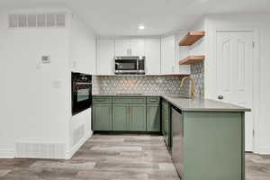 Kitchen featuring light wood-type flooring, green cabinets, white cabinetry, sink, and appliances with stainless steel finishes