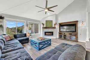 Living room with high vaulted ceiling, ceiling fan, a tile fireplace, and light hardwood / wood-style floors