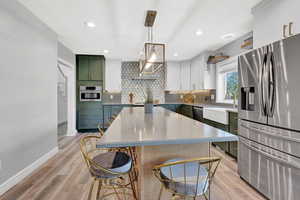 Kitchen with decorative light fixtures, a kitchen bar, stainless steel appliances, and light hardwood / wood-style flooring