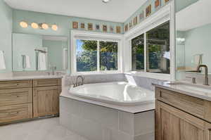 Bathroom featuring tile patterned flooring, tiled tub, and vanity