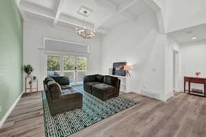 Living room with coffered ceiling, beamed ceiling, a chandelier, and light hardwood / wood-style floors