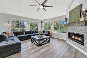 Living room with ceiling fan, a tiled fireplace, light hardwood / wood-style floors, and vaulted ceiling