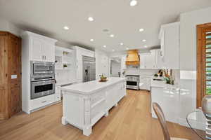 Kitchen featuring built in appliances, a center island, custom exhaust hood, light wood-type flooring, and white cabinets