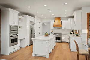 Kitchen with built in appliances, premium range hood, a kitchen island, and light hardwood / wood-style flooring