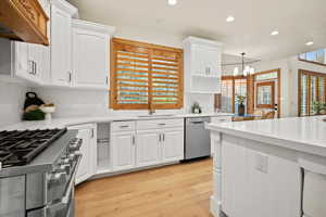 Kitchen featuring custom range hood, light hardwood / wood-style flooring, stainless steel appliances, white cabinetry, and pendant lighting