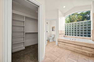 Bathroom featuring vaulted ceiling, toilet, a relaxing tiled tub, and tile patterned flooring