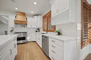 Kitchen with appliances with stainless steel finishes, light hardwood / wood-style floors, white cabinetry, sink, and premium range hood