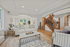 Living room featuring light wood-type flooring, ornamental molding, a chandelier, and a tray ceiling