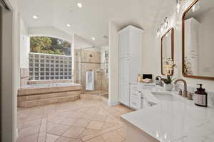 Bathroom with vanity, vaulted ceiling, tile patterned floors, and shower with separate bathtub