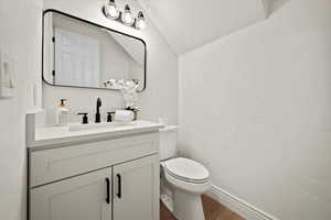 Bathroom featuring a textured ceiling, vanity, vaulted ceiling, wood-type flooring, and toilet