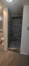 Bathroom with a textured ceiling, a shower, and toilet