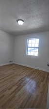 Empty room featuring a textured ceiling and dark hardwood / wood-style floors