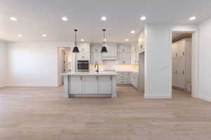 Kitchen featuring white cabinetry, light hardwood / wood-style flooring, decorative light fixtures, oven, and a center island with sink