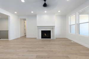 Unfurnished living room with a fireplace, plenty of natural light, ceiling fan, and light hardwood / wood-style floors