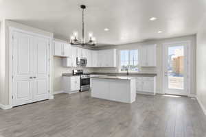 Kitchen featuring white cabinetry, light hardwood / wood-style flooring, decorative light fixtures, and stainless steel appliances