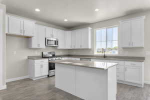 Kitchen featuring white cabinets, light wood-type flooring, stainless steel appliances, sink, and a kitchen island