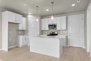 Kitchen featuring appliances with stainless steel finishes, light hardwood / wood-style floors, an island with sink, sink, and white cabinetry