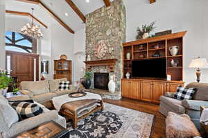 Living room featuring hardwood / wood-style flooring, a fireplace, a notable chandelier, beamed ceiling, and high vaulted ceiling