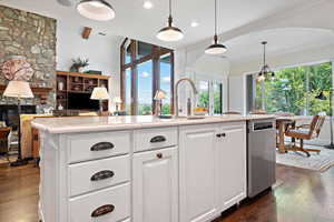 Kitchen with dark wood-type flooring, white cabinetry, pendant lighting, and a stone fireplace