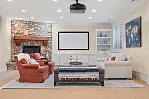 Carpeted home theater with crown molding, built in shelves, and a stone fireplace