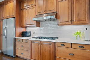 Kitchen featuring dark wood-type flooring, stainless steel appliances, light stone counters, and tasteful backsplash