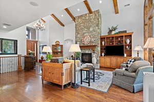 Living room with an inviting chandelier, beamed ceiling, a stone fireplace, hardwood / wood-style floors, and high vaulted ceiling