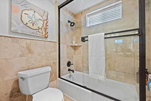 Bathroom featuring tile walls, toilet, and combined bath / shower with glass door