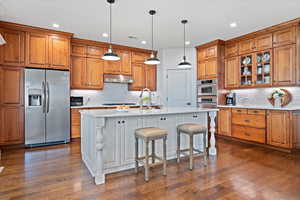 Kitchen with tasteful backsplash, a kitchen breakfast bar, dark hardwood / wood-style floors, appliances with stainless steel finishes, and a center island with sink