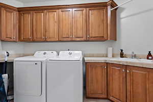 Clothes washing area with cabinets, washer and clothes dryer, and sink