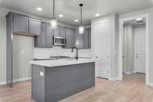 Kitchen with a center island with sink, pendant lighting, light hardwood / wood-style floors, stainless steel appliances, and gray cabinets