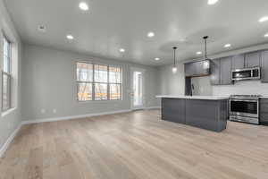 Kitchen featuring light wood-type flooring, stainless steel appliances, a center island, hanging light fixtures, and gray cabinetry