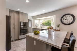 Kitchen featuring a breakfast bar, stainless steel appliances, light stone counters, and gray cabinets