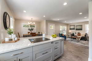 Kitchen with light wood-type flooring, light stone countertops, black electric cooktop, and a notable chandelier