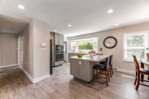 Kitchen with light hardwood / wood-style flooring, stainless steel appliances, gray cabinetry, and a breakfast bar area