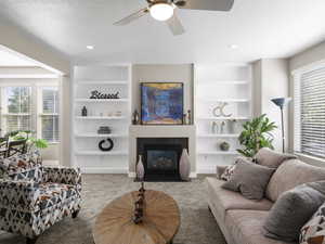 Living room with built in shelves, plenty of natural light, and ceiling fan