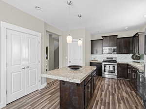 Kitchen with a kitchen island, dark hardwood / wood-style floors, pendant lighting, appliances with stainless steel finishes, and decorative backsplash