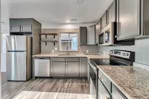 Kitchen with gray cabinets, stainless steel appliances, light hardwood / wood-style floors, and sink