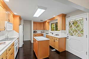 Kitchen featuring white appliances, a center island, dark wood-type flooring, sink, and light brown cabinets