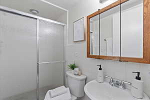 Bathroom featuring toilet, sink, tile walls, a shower with shower door