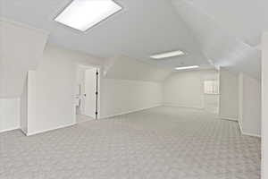 Bonus room with light colored carpet and vaulted ceiling