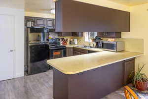 Kitchen with light  wood-style floors, sink, black appliances, kitchen peninsula, and ceiling fan