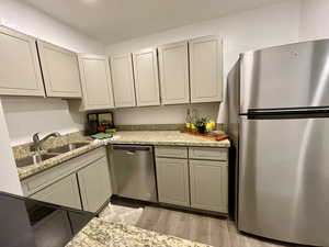 Kitchen with light stone counters, sink, stainless steel appliances, and light hardwood / wood-style floors