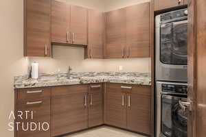 Kitchen with light stone counters, sink, and stacked washing maching and dryer