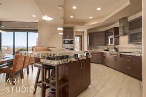 Kitchen featuring a wealth of natural light, stainless steel gas stovetop, light stone countertops, and dark brown cabinetry