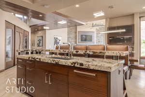 Kitchen featuring light tile patterned floors, decorative light fixtures, light stone counters, a center island, and sink